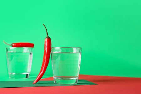 Glasses of water and chili pepper on color background