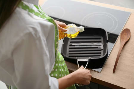 Woman pouring sunflower oil onto frying pan in kitchenの写真素材