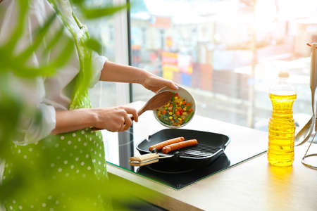 Woman cooking vegetables and sausages in kitchenの写真素材