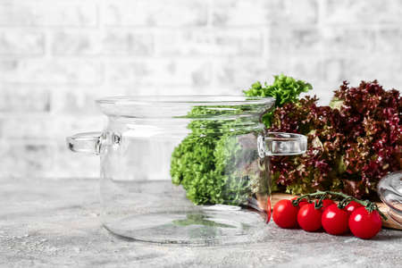 Stylish cooking pot and vegetables on table against brick wallの写真素材