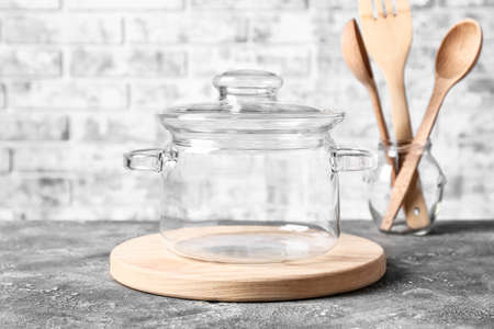 Stylish cooking pot and utensils on table against brick wallの写真素材