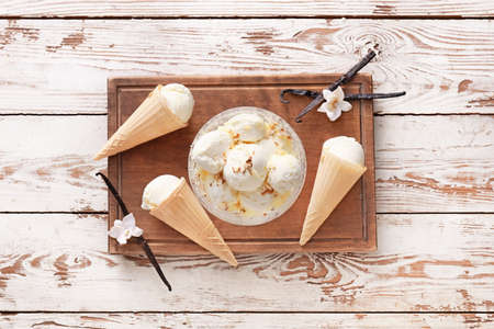 Board with tasty vanilla ice cream on light wooden background