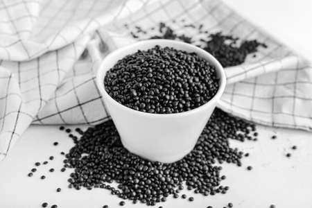 Bowl with black lentils on light background