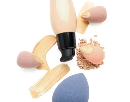 Bottle of makeup foundation, sponges and samples on white background, closeup