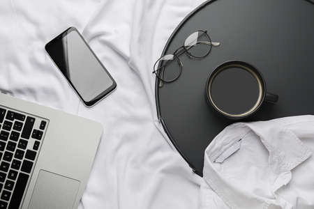 Composition with cup of coffee and mobile phone on bed