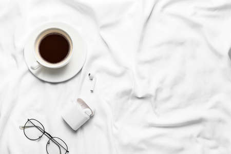 Cup of coffee with earphones and glasses on bedの写真素材