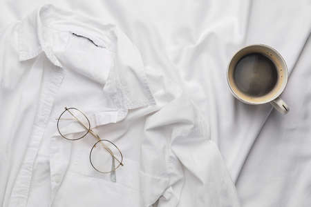 Cup of coffee with shirt and glasses on bedの写真素材