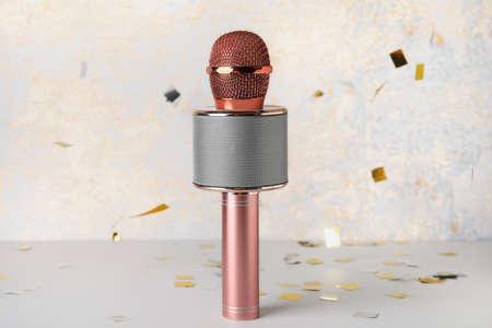 Modern microphone and confetti on light background