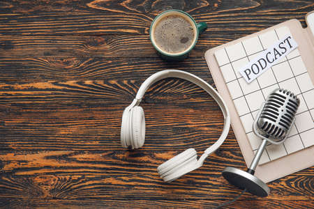 Retro microphone, headphones, paper with word PODCAST and cup of coffee on wooden backgroundの写真素材