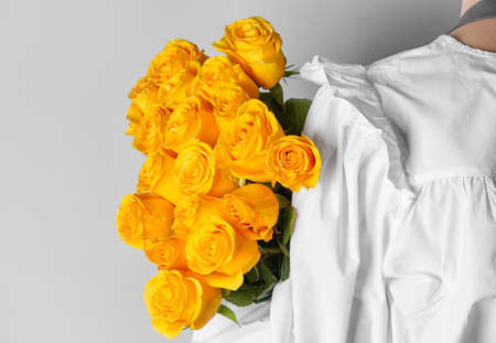 Young woman with beautiful yellow roses on light background, back view