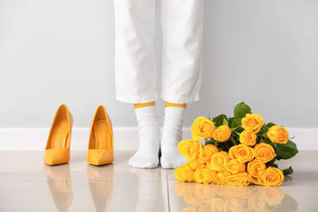 Stylish young woman with beautiful yellow roses and high-heels near light wallの写真素材