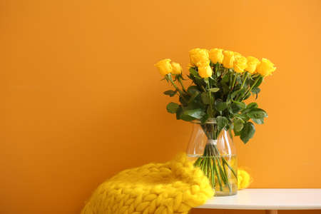 Vase with beautiful yellow roses on table near color wall in roomの写真素材