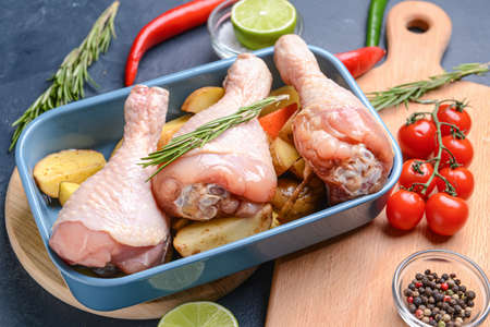 Baking dish with raw chicken legs and potato on dark background