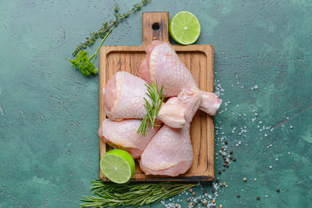 Board with raw chicken legs on color background
