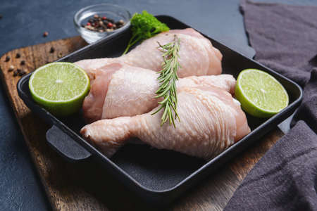 Baking dish with raw chicken legs on dark background