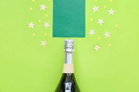 Bottle of champagne with paper sheet and confetti on color backgroundの写真素材
