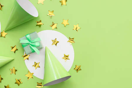 Gift box with party hats and confetti on color background