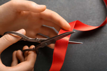 Woman cutting red ribbon on dark background, closeupの写真素材