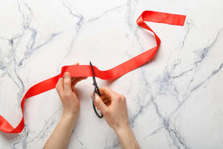 Woman cutting red ribbon on light backgroundの写真素材