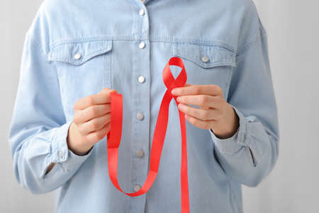 Woman holding red ribbon on light background. AIDS awareness concept