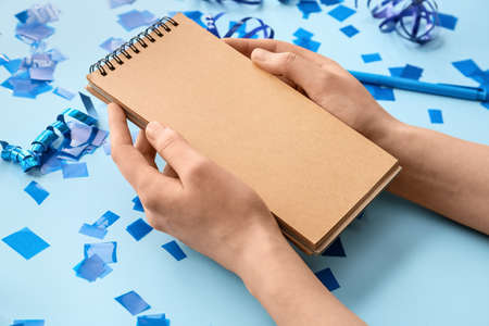 Female hands with blank notebook and confetti on color background