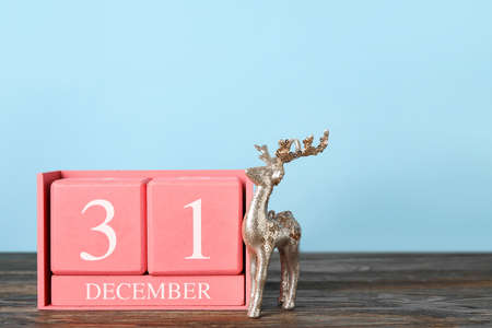 Calendar with date of New Year and toy reindeer on table against color background