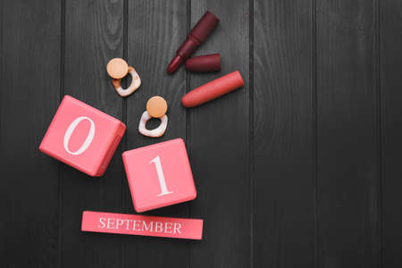 Calendar with date of September 1, earrings and lipsticks on dark wooden background