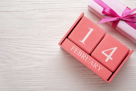 Calendar with date of Valentines Day and gift box on light wooden background