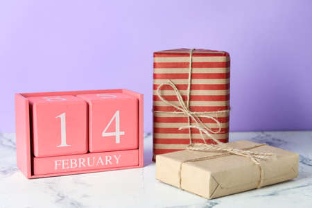 Calendar with date of Valentines Day and gift boxes on table against color background