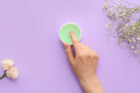 Woman with hand cream on color background
