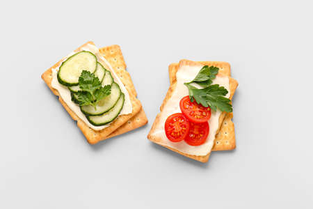 Tasty crackers with cheese, tomatoes and cucumber on gray background