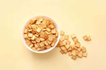 Bowl with tasty crackers on color background