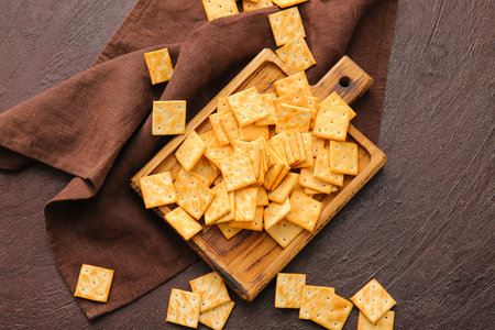 Board with tasty crackers on dark background