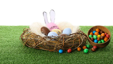 Nest with Easter eggs on grass against white background