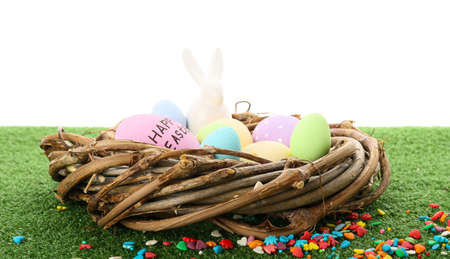Nest with Easter eggs on grass against white background