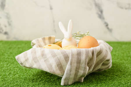 Easter eggs and figurine of rabbit on grass against light backgroundの写真素材