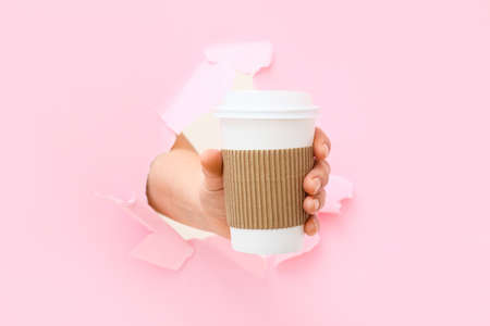 Woman with takeaway cup for coffee visible through hole in torn color paperの写真素材