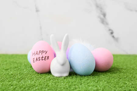 Easter eggs and figurine of rabbit on grass against light background