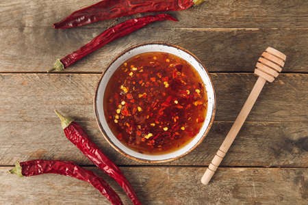 Bowl of hot honey and dry chili peppers on wooden backgroundの写真素材