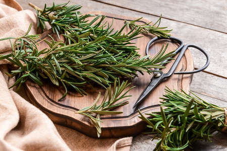 Board with fresh rosemary and scissors on wooden background, closeupの写真素材