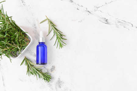 Bottle of essential oil and fresh rosemary on light backgroundの写真素材