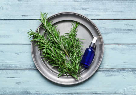Tray with essential oil and fresh rosemary on color wooden backgroundの写真素材