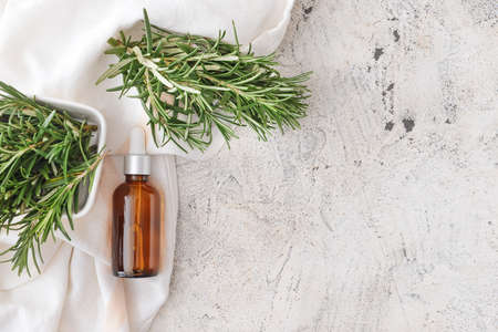 Bottle of essential oil and fresh rosemary on light backgroundの写真素材