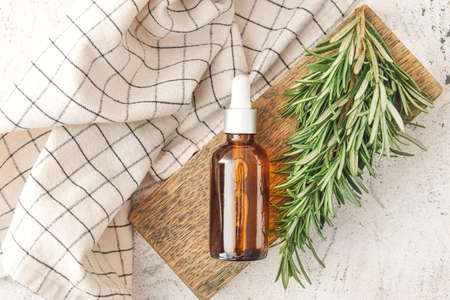 Bottle of essential oil and fresh rosemary on light backgroundの写真素材