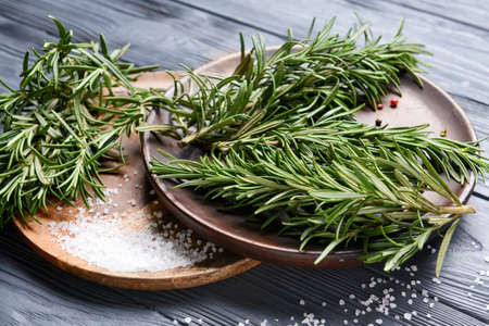 Plates with fresh rosemary and spices on dark wooden background, closeupの写真素材
