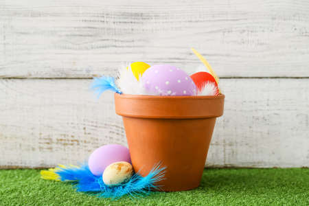 Pot with beautiful Easter eggs on grass against light backgroundの写真素材