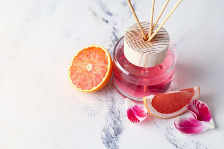 Reed diffuser with citrus and flower petals on light background