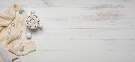 Children's sweater with cup of hot chocolate on white wooden background with space for text