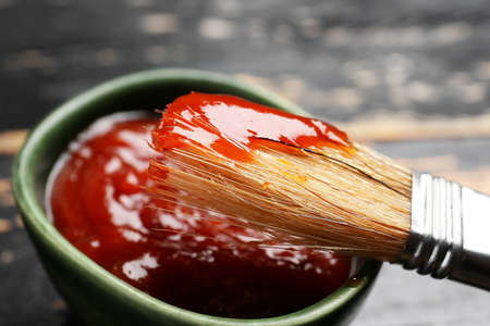 Bowl with tasty barbecue sauce and brush on dark wooden background, closeupの写真素材