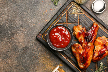 Board with roasted chicken wings and barbecue sauce on grunge backgroundの写真素材